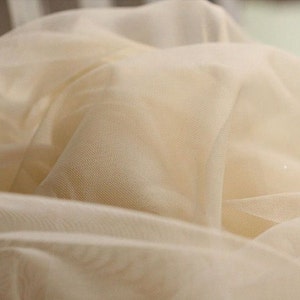 May include: Close-up of a soft, ivory-coloured tulle fabric. The fabric is sheer and delicate, with a fine mesh weave.