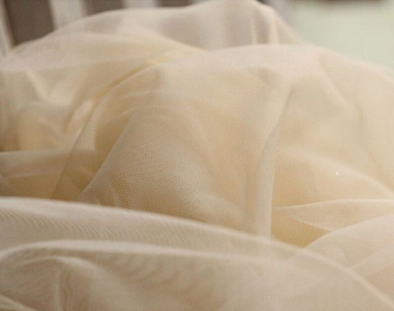 May include: Close-up of a soft, ivory-coloured tulle fabric. The fabric is sheer and delicate, with a fine mesh weave.