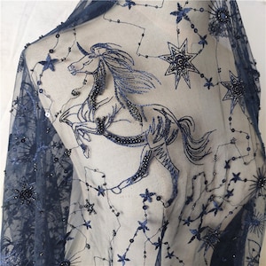 May include: Navy blue sheer fabric with embroidered stars and a unicorn design. The fabric is embellished with black beads.