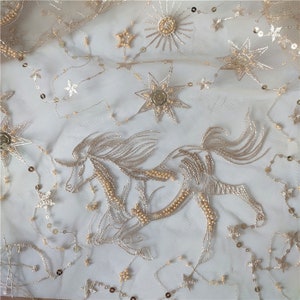May include: Gold embroidered tulle fabric with a unicorn and stars design. The fabric is sheer and has a delicate texture.