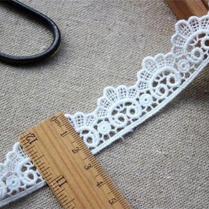 May include: White lace trim with a delicate floral pattern. The trim is approximately 4 inches wide and is measured with a ruler.