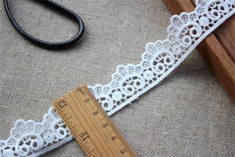 May include: White lace trim with a delicate floral pattern. The trim is approximately 4 inches wide and is measured with a ruler.