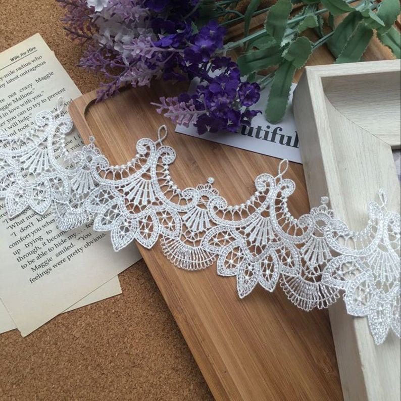 May include: White lace trim with a delicate floral pattern. The lace is about 2 inches wide and has a scalloped edge.