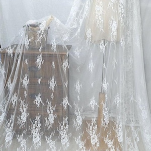 Könnte beinhalten: Weißer floraler Spitzenstoff mit einem zarten Muster. Die Spitze hat einen gewellten Rand und ist über eine Schaufensterpuppe drapiert.