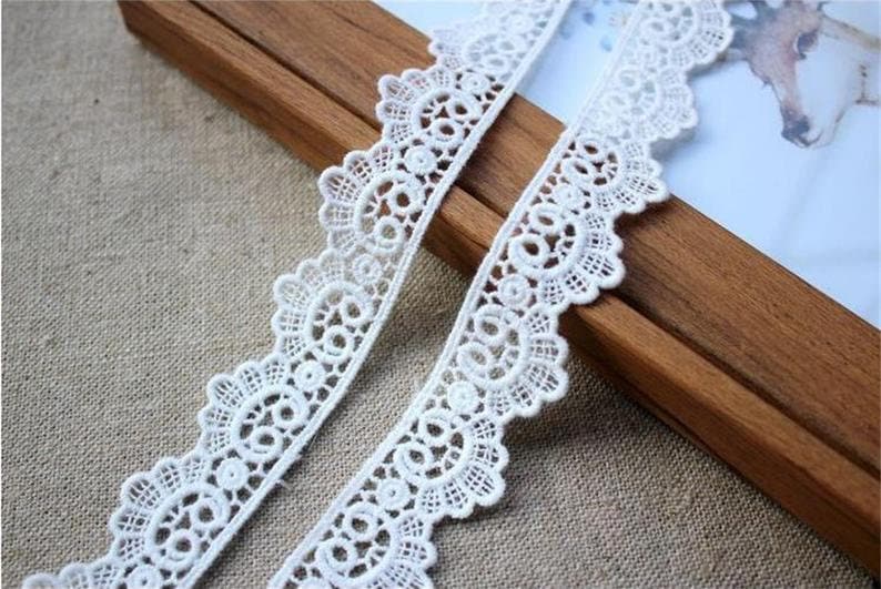 May include: White lace trim with a scalloped edge and delicate floral pattern. The lace is approximately 2.5 cm wide.