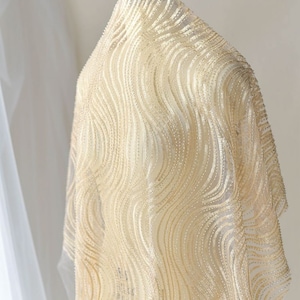 Puede incluir: Primer plano de una tela dorada con un patrón ondulado. La tela es transparente y tiene un brillo sutil.