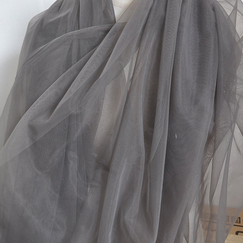 Pu&ograve; includere: Tessuto di tulle grigio trasparente, un materiale leggero e delicato spesso utilizzato per progetti di artigianato e cucito.