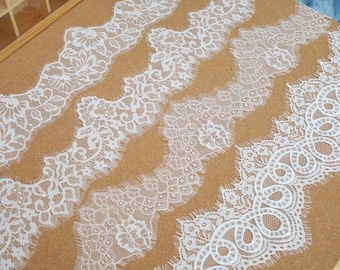 May include: Several white lace trims with various floral and geometric patterns are displayed on a brown surface. The lace trims have scalloped edges and intricate designs, perfect for crafting and sewing projects.