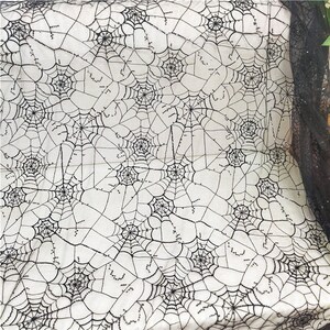 May include: A black spiderweb patterned fabric featuring intricate web designs with small, reflective black sequins stitched along the lines. The sheer, lightweight material displays a repeating pattern of interconnected webs across the surface.