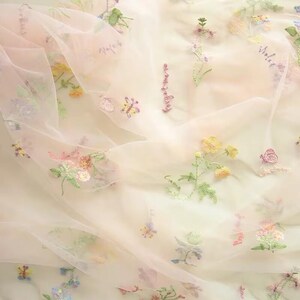 May include: Delicate pink tulle fabric with embroidered floral designs in shades of pink, yellow, green, and blue. The fabric features small butterflies and the words "sweet" and "violet" embroidered in a cursive font.