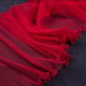 Peut inclure: Un tissu pliss&eacute; rouge vif avec un bord d&eacute;licat et fronc&eacute;. Le mat&eacute;riau semble l&eacute;ger et fluide, avec de subtiles lignes verticales ajoutant de la texture. Id&eacute;al pour les v&ecirc;tements ou la d&eacute;coration.