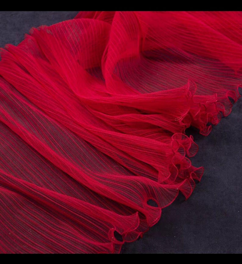 Peut inclure: Un tissu pliss&eacute; rouge vif avec un bord d&eacute;licat et fronc&eacute;. Le mat&eacute;riau semble l&eacute;ger et fluide, avec de subtiles lignes verticales ajoutant de la texture. Id&eacute;al pour les v&ecirc;tements ou la d&eacute;coration.