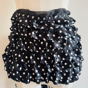 May include: Black and white polka dot ruffle skirt with multiple layers. The skirt is made of a satin-like fabric.