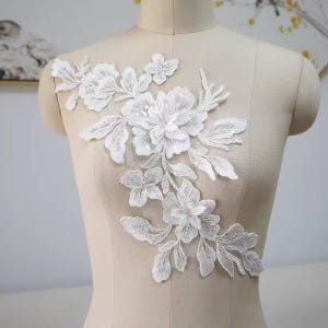 Puede incluir: Aplicación de encaje floral blanco con diseños detallados de flores y hojas. La aplicación está hecha de encaje delicado y es ideal para embellecer prendas o proyectos de manualidades. El diseño incluye flores y hojas de varios tamaños.
