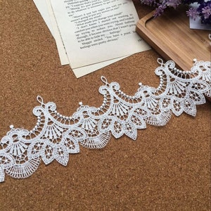 May include: White lace trim with a delicate floral pattern. The lace is made of a fine, lightweight material and has a scalloped edge.