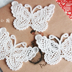 May include: Three white lace butterfly appliques. The butterflies are delicate and intricate, with a fine, openwork design.