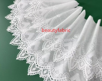 Könnte beinhalten: Weiße Baumwollspitzenborte mit zartem Blumenmuster. Die Spitze hat einen gewellten Rand und ist perfekt, um jedem Projekt einen Hauch von Eleganz zu verleihen.