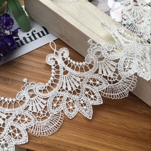 May include: White lace trim with a delicate floral pattern and small pearl accents. The lace is soft and flowing, making it perfect for adding a touch of elegance to any project.