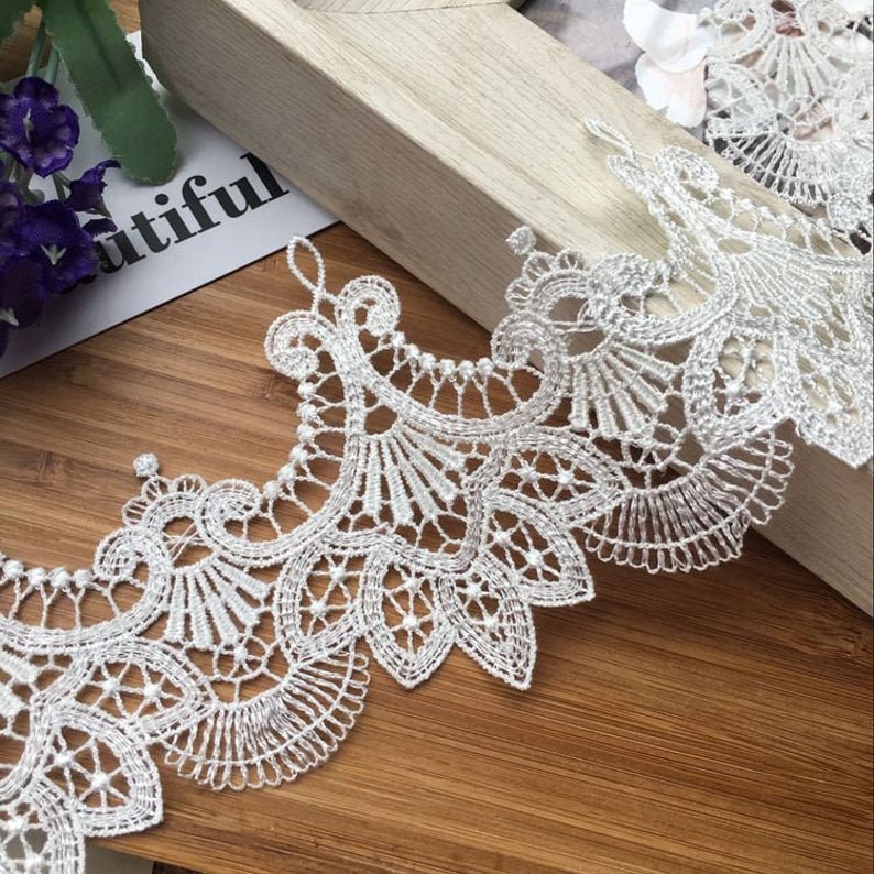 May include: White lace trim with a delicate floral pattern and small pearl accents. The lace is soft and flowing, making it perfect for adding a touch of elegance to any project.