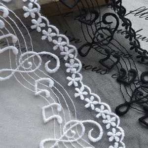 May include: Two pieces of black and white lace trim featuring a musical note design. The lace is delicate and has a scalloped edge.
