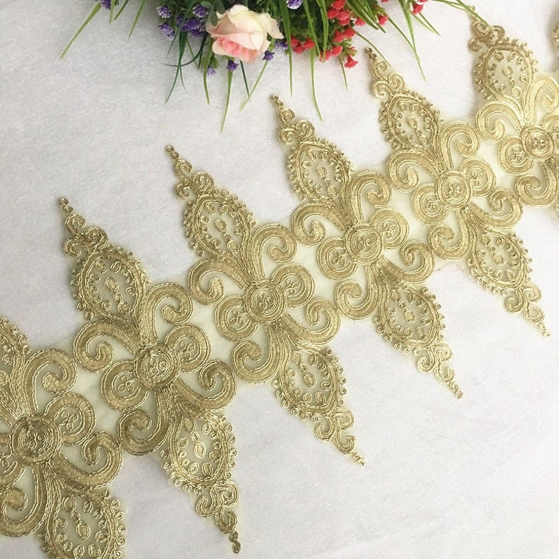 K&ouml;nnte beinhalten: Goldene Spitzenborte mit einem gewellten Rand und filigranen Blumenmustern. Die Spitze ist zart und hat eine weiche, flie&szlig;ende Textur.