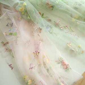 May include: Pale green and pink sheer fabric with embroidered flowers and butterflies. The fabric has a delicate, romantic feel.