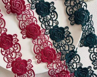 May include: Close-up of decorative lace trim featuring floral rose designs. The lace is available in two colors: deep red and dark teal. The intricate patterns and delicate details make this trim suitable for various craft projects.
