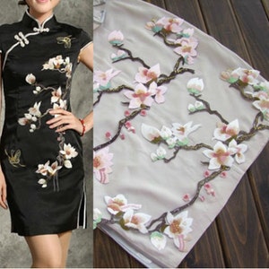 May include: A beige fabric with a floral design featuring white and pink flowers with green leaves. The flowers are embroidered and have a 3D effect.