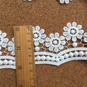 May include: White lace trim with a scalloped edge and a repeating floral pattern. The lace is approximately 2.5 inches wide.