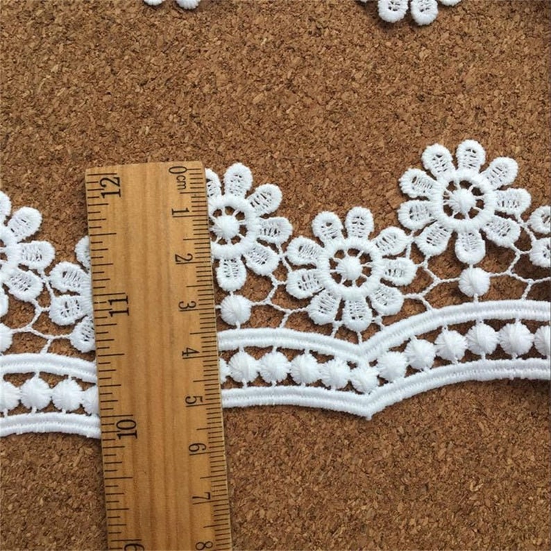 May include: White lace trim with a scalloped edge and a repeating floral pattern. The lace is approximately 2.5 inches wide.