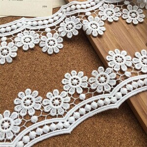 May include: White lace trim with a scalloped edge and small white pom-poms. The lace features a repeating pattern of delicate flowers.