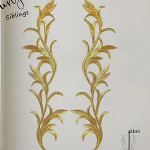 May include: Two gold embroidered floral appliques. Each applique features a detailed design of leaves and stems. The appliques are approximately 33cm in height and 9cm in width. The word "Siblings" is written in cursive in the upper left corner.
