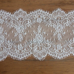 Op de afbeelding: Wit kantlint met een gegolfde rand en ingewikkelde bloemmotieven.