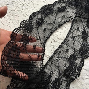 Op de afbeelding: Zwarte kantbies met een gegolfde rand en een geplisseerd ontwerp. De kant is delicaat en doorschijnend, met een bloemenpatroon.