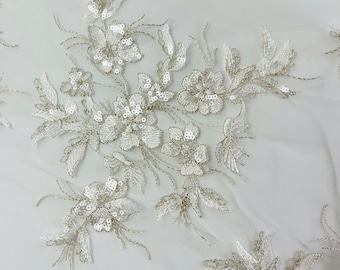 May include: White floral lace fabric with silver sequins. The lace features a delicate floral pattern with small, shimmering sequins.