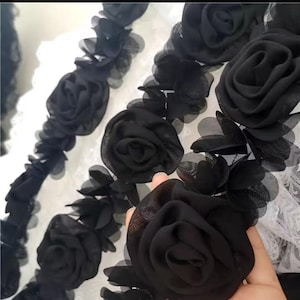 Pode incluir: Close-up de enfeites florais de tecido preto. A imagem mostra várias rosas de tecido preto com pétalas e folhas detalhadas. As rosas são dispostas em um padrão decorativo, adequado para artesanato ou roupas.