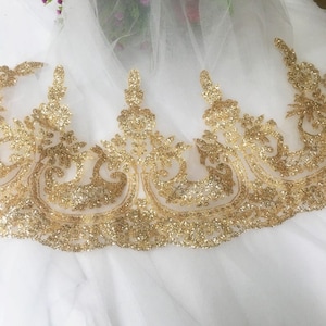 Peut inclure: Garniture de dentelle dorée à paillettes avec un motif floral délicat. La dentelle est sur un fond de tulle blanc.