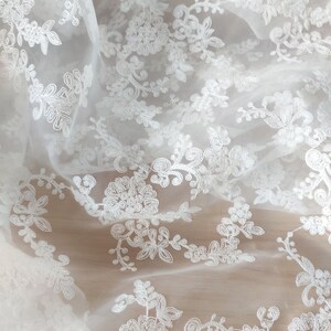 May include: White sheer fabric with a delicate floral embroidery pattern.