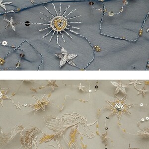 May include: Close-up of two fabrics with embroidered celestial designs. One is navy blue with silver stars, suns, and sequins. The other is beige with a unicorn and star patterns, also with sequins and gold beads. Ideal for apparel or decor.