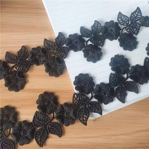 Op de afbeelding: Zwarte bloemen kanten rand met gedetailleerde bloemen- en bladerenpatronen. De rand is gemaakt van een fijne, open geweven stof, ideaal om een vleugje elegantie toe te voegen aan knutselprojecten. Perfect voor het verfraaien van kleding, accessoires of woondecoratie.