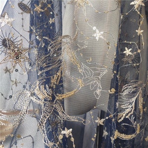 May include: Black mesh fabric with gold embroidery of stars and floral designs. The fabric is sheer and has a delicate texture.