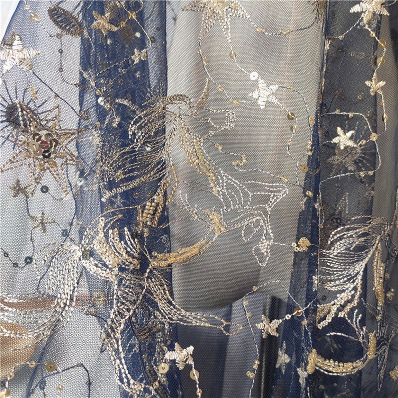 May include: Black mesh fabric with gold embroidery of stars and floral designs. The fabric is sheer and has a delicate texture.