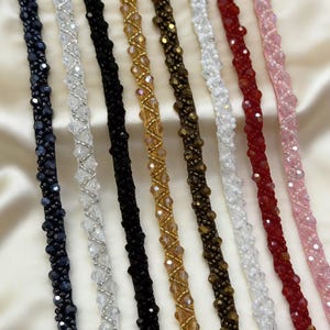 May include: Close-up of multiple beaded strands in various colors, including black, silver, gold, brown, white, red, and pink. Each strand is intricately designed with small, sparkling beads, creating a textured and decorative effect. The beads are arranged in a repeating pattern.