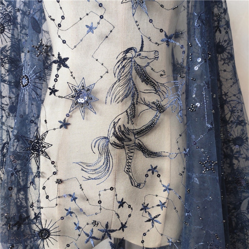 May include: Navy blue tulle fabric with a black embroidered unicorn and stars. The fabric is embellished with sequins.