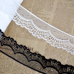 Könnte beinhalten: Zwei Spitzenbänder, eines schwarz und eines weiß, mit gewellten Kanten und filigranen Mustern. Die Bänder liegen auf einem Zeitungspapier-Hintergrund.