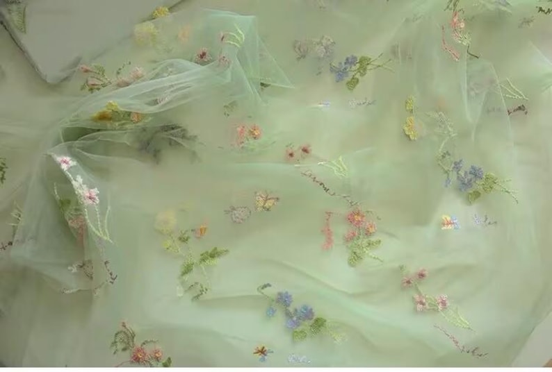 May include: Pale green tulle fabric with embroidered flowers in shades of pink, yellow, blue, and green.