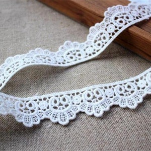 May include: White lace trim with a scalloped edge and delicate floral pattern. The lace is approximately 2.5 cm wide.