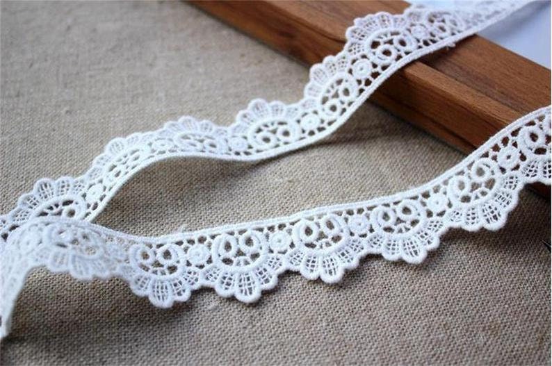 May include: White lace trim with a scalloped edge and delicate floral pattern. The lace is approximately 2.5 cm wide.