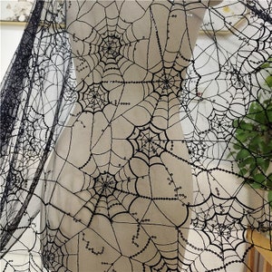 May include: A sheer black fabric featuring an intricate embroidered spider web pattern. The design consists of multiple interconnected webs with black thread and small, reflective black sequins stitched along the lines of the web structure.
