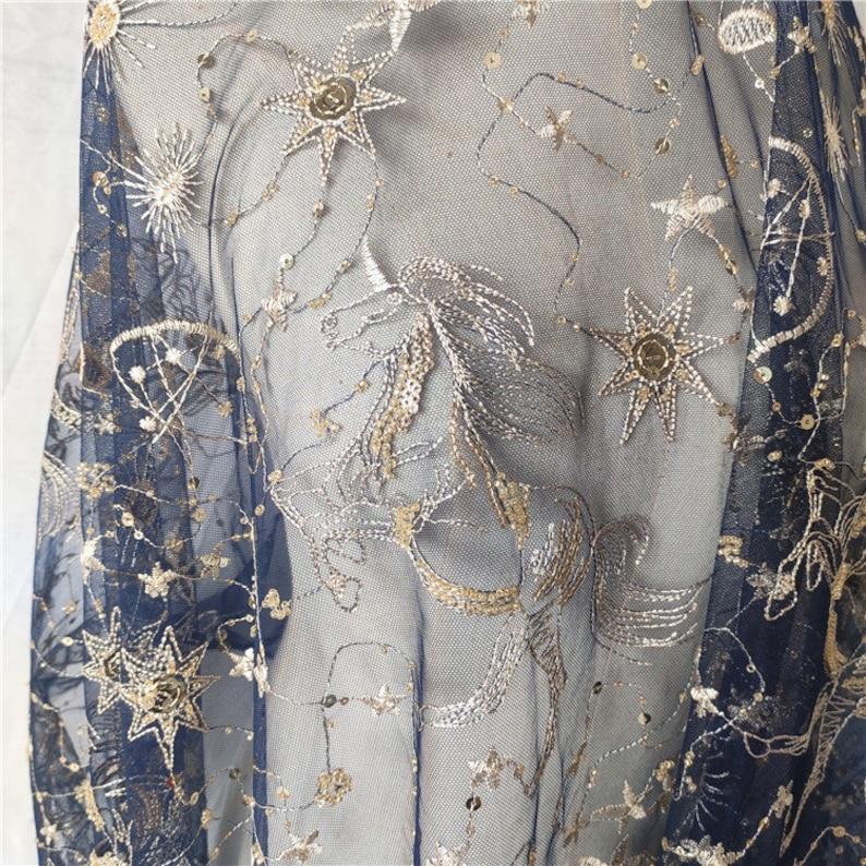 May include: Navy blue sheer fabric with gold and silver embroidered stars and constellations. The fabric is delicate and has a soft, flowing texture.